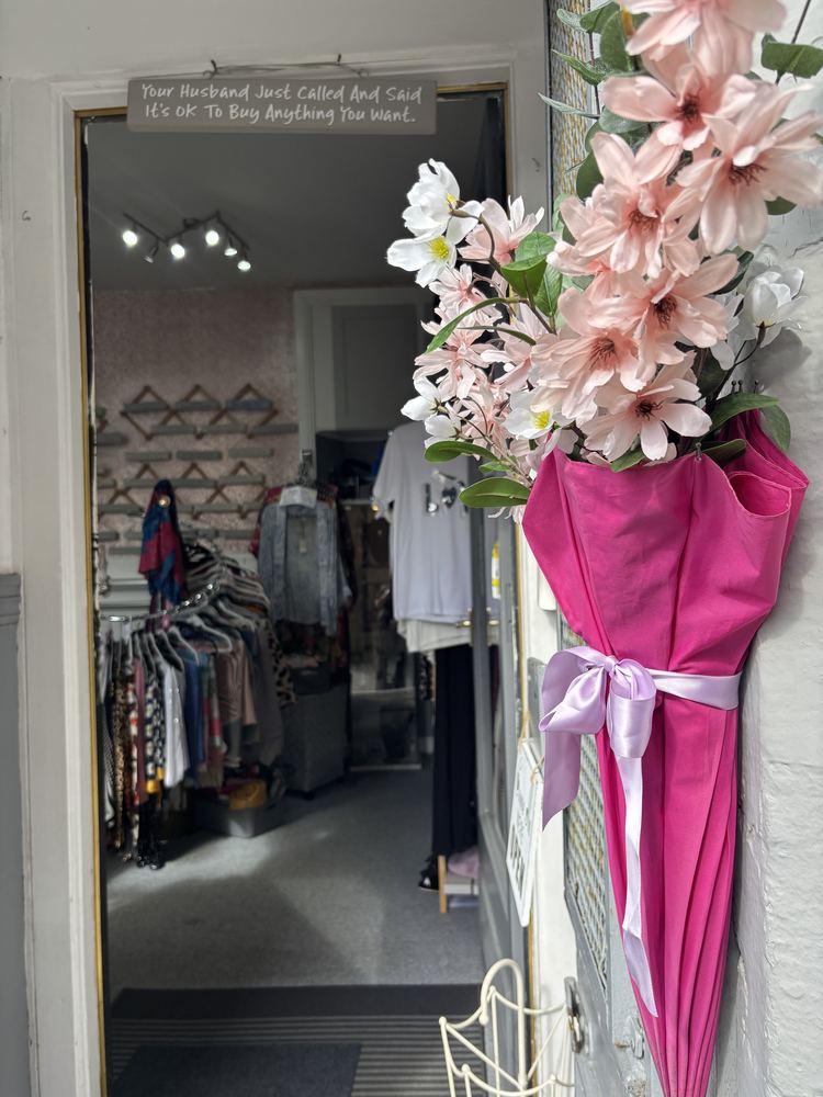 A bright pink umbrella tied with a lilac ribbon, hanging in the shop doorway